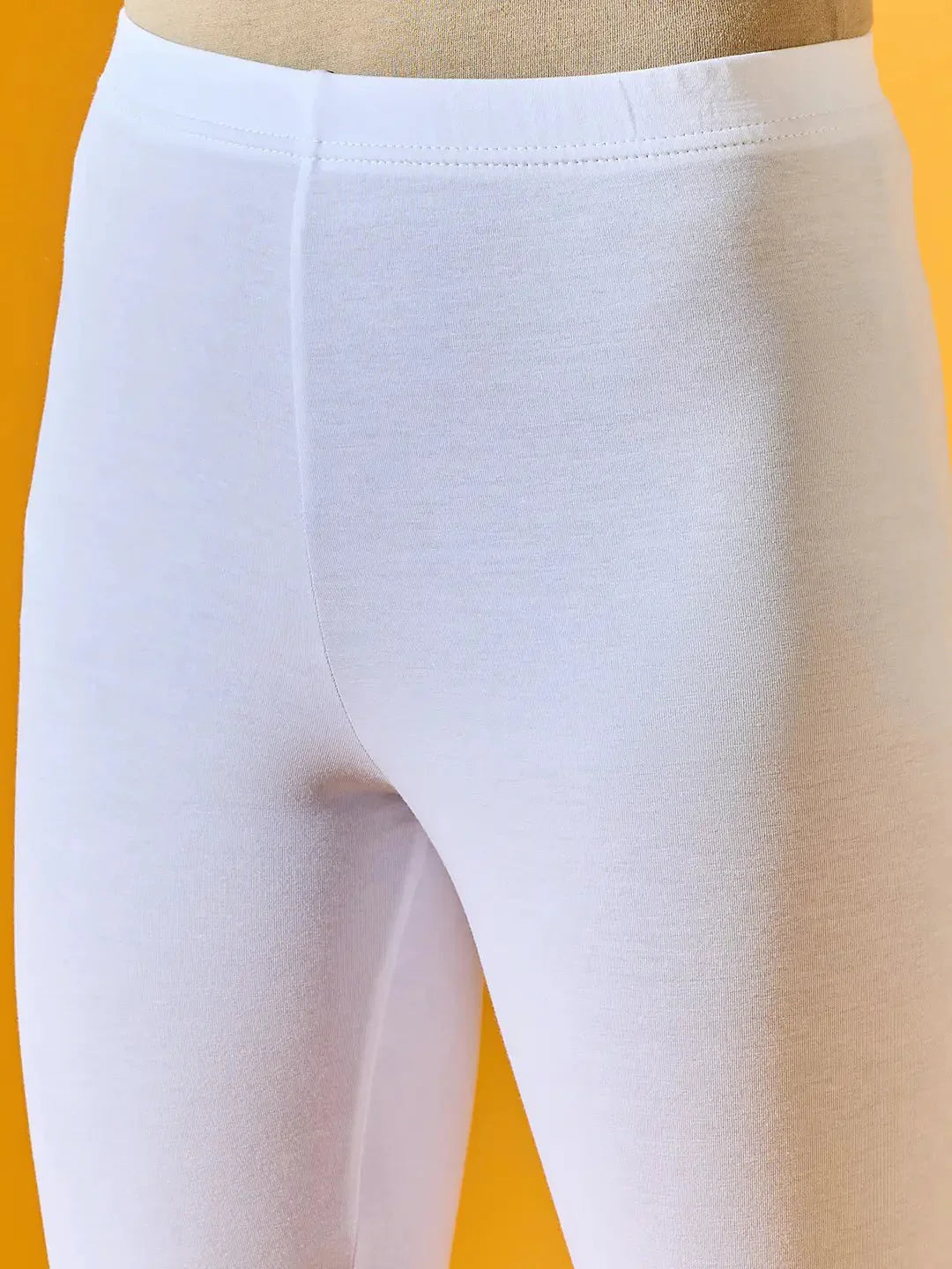Close-up of a person wearing 98degreenorth Women White Ankle-Length Leggings against a yellow background.