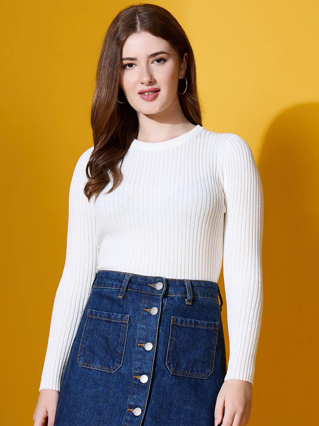 Woman in a 98degreenorth white ribbed sweater, styled with a denim skirt, posing against a yellow background.