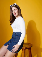 Woman in 98degreenorth White Ribbed Sweater and denim skirt sits on a stool, wearing white sunglasses.