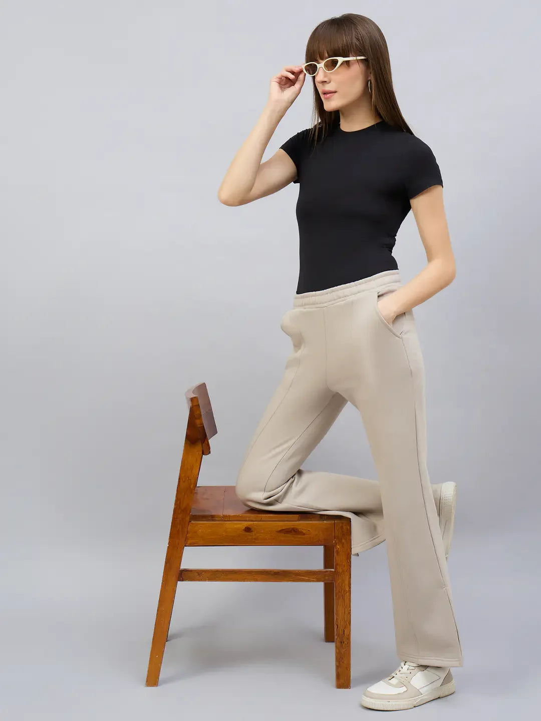 A woman in 98degreenorth almond flared bootcut sweatpants poses with one leg on a chair, adjusting her sunglasses.