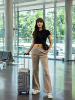 A woman stands in an airport, smiling in 98degreenorth Women’s Almond Fleece Flared Sweatpants, suitcase by her side.