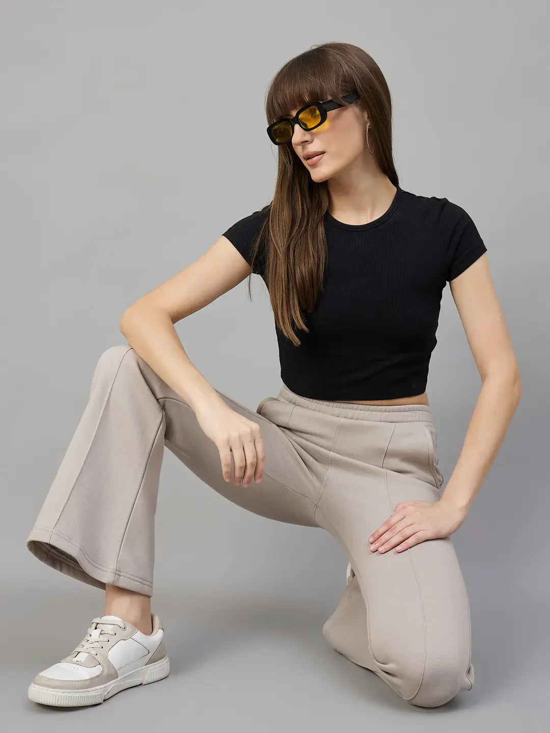 Model in 98degreenorth Women’s Almond Fleece Flared Sweatpants kneels in sunglasses against a gray background.
