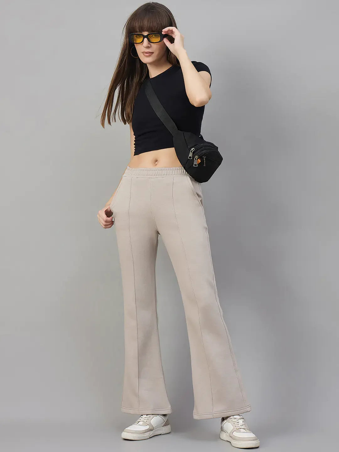 Woman in black crop top, 98degreenorth Almond Fleece Flared Sweatpants, white sneakers, sunglasses, crossbody bag.