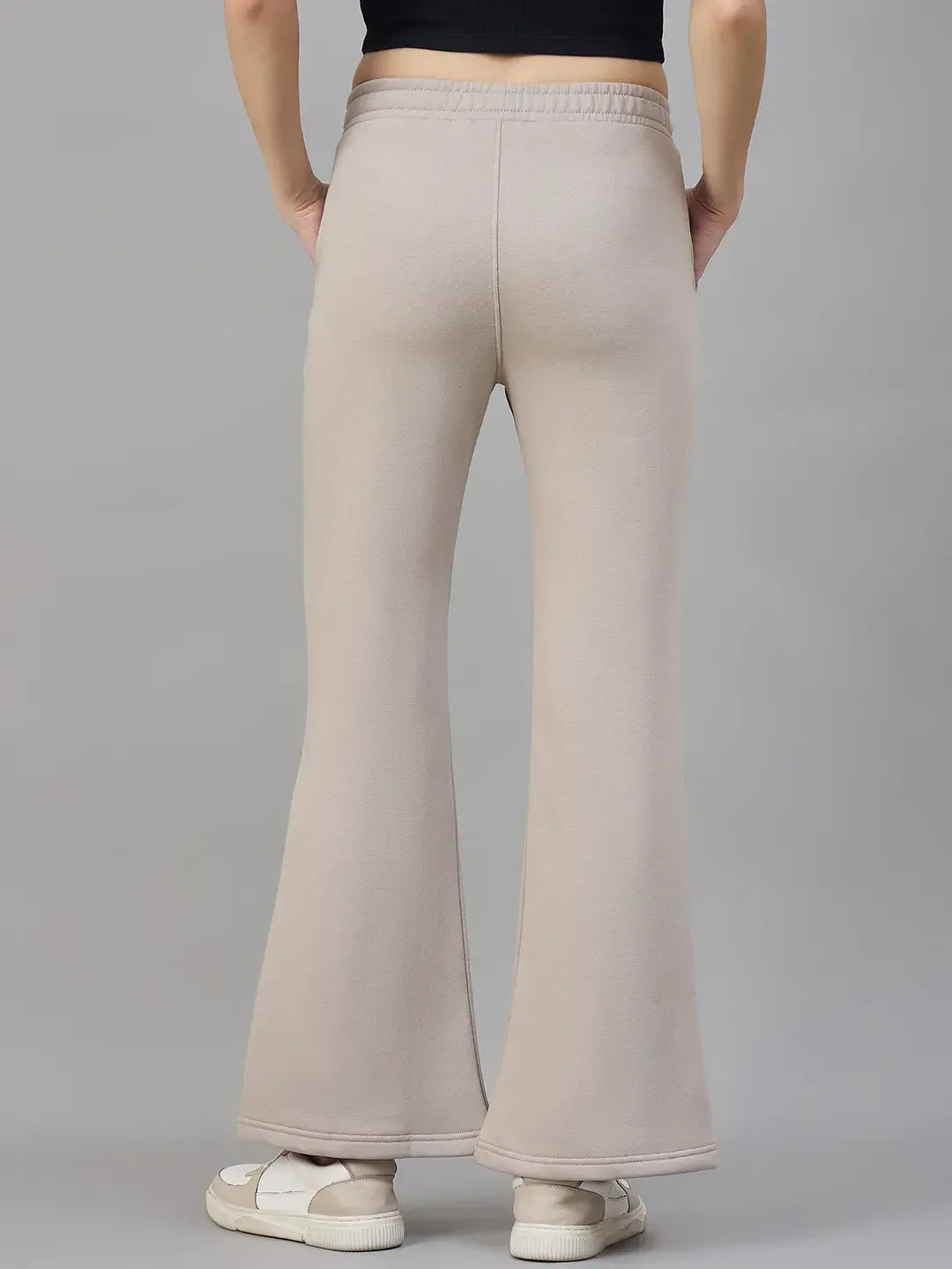 Woman in 98degreenorth high waist Almond Fleece Flared Sweatpants, shown from the back against a gray background.