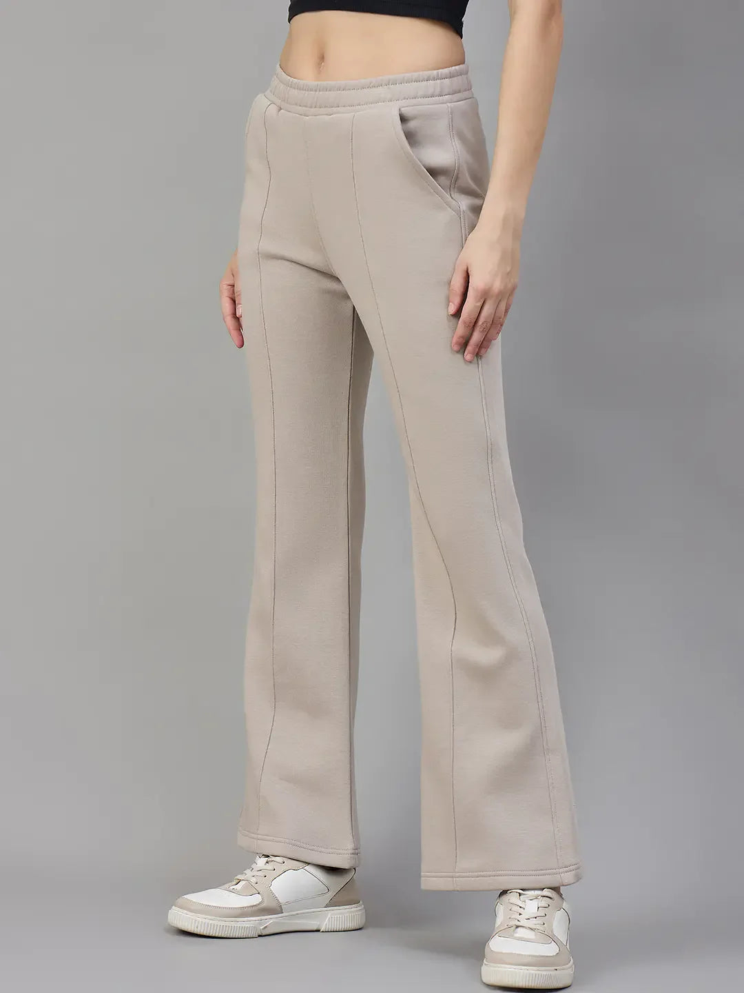 A person wears 98degreenorth Women’s Almond Fleece Flared Sweatpants, white sneakers, and a black crop top.