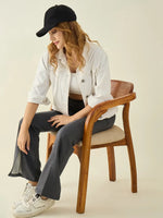 A woman in a white jacket and black cap smiles, wearing 98degreenorth anthra flared bootcut sweatpants with side slit.