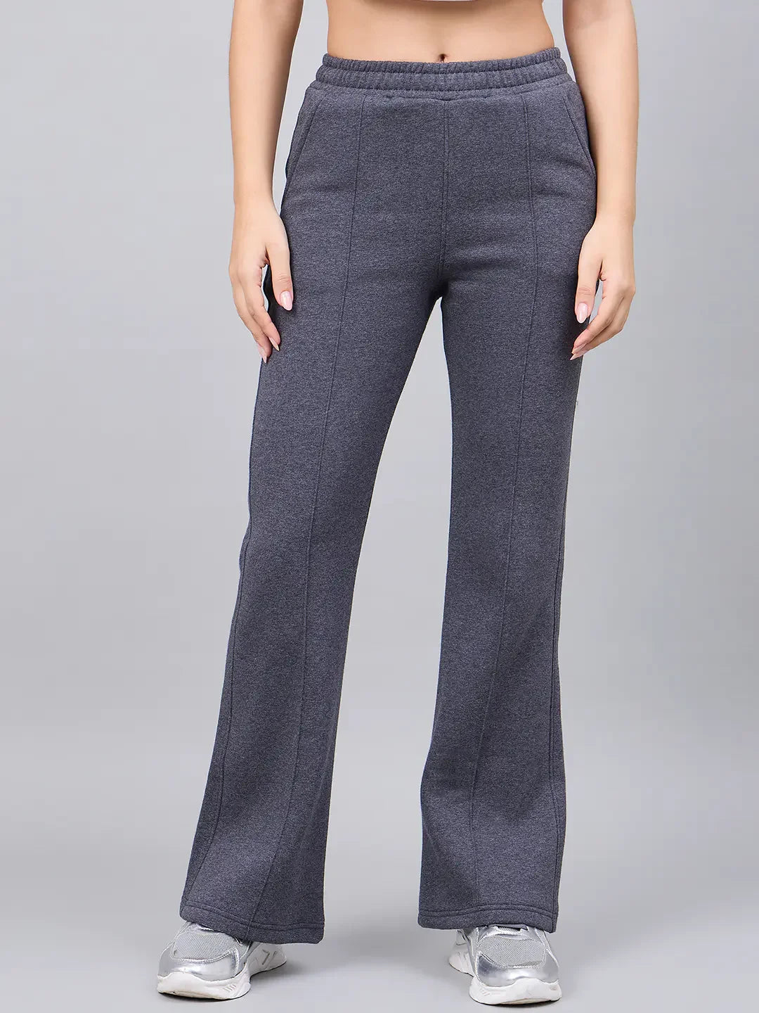 Model in 98degreenorth Women’s Anthra Fleece Flared Sweatpants with white sneakers, posing against a gray background.