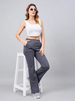 A woman in sunglasses wears 98degreenorth Women’s Anthra Fleece Flared Sweatpants, leaning on a stool against a gray background.