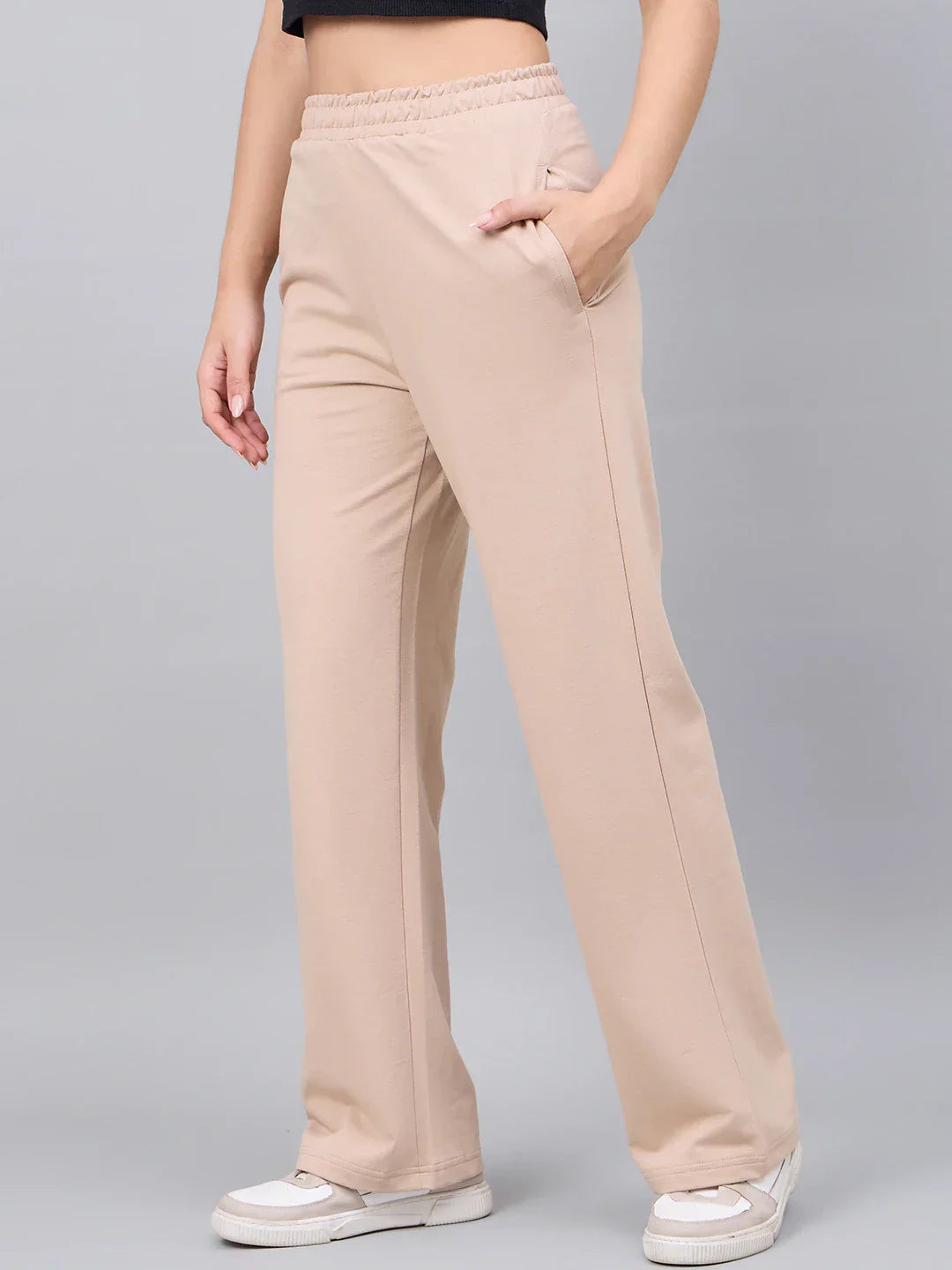 A person wears 98degreenorth Women’s Beige Cotton Stretchable Trackpants, a black crop top, and white sneakers.