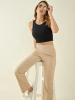 Woman in 98degreenorth high waist beige trackpants and black crop top sits stylishly against a gray background.