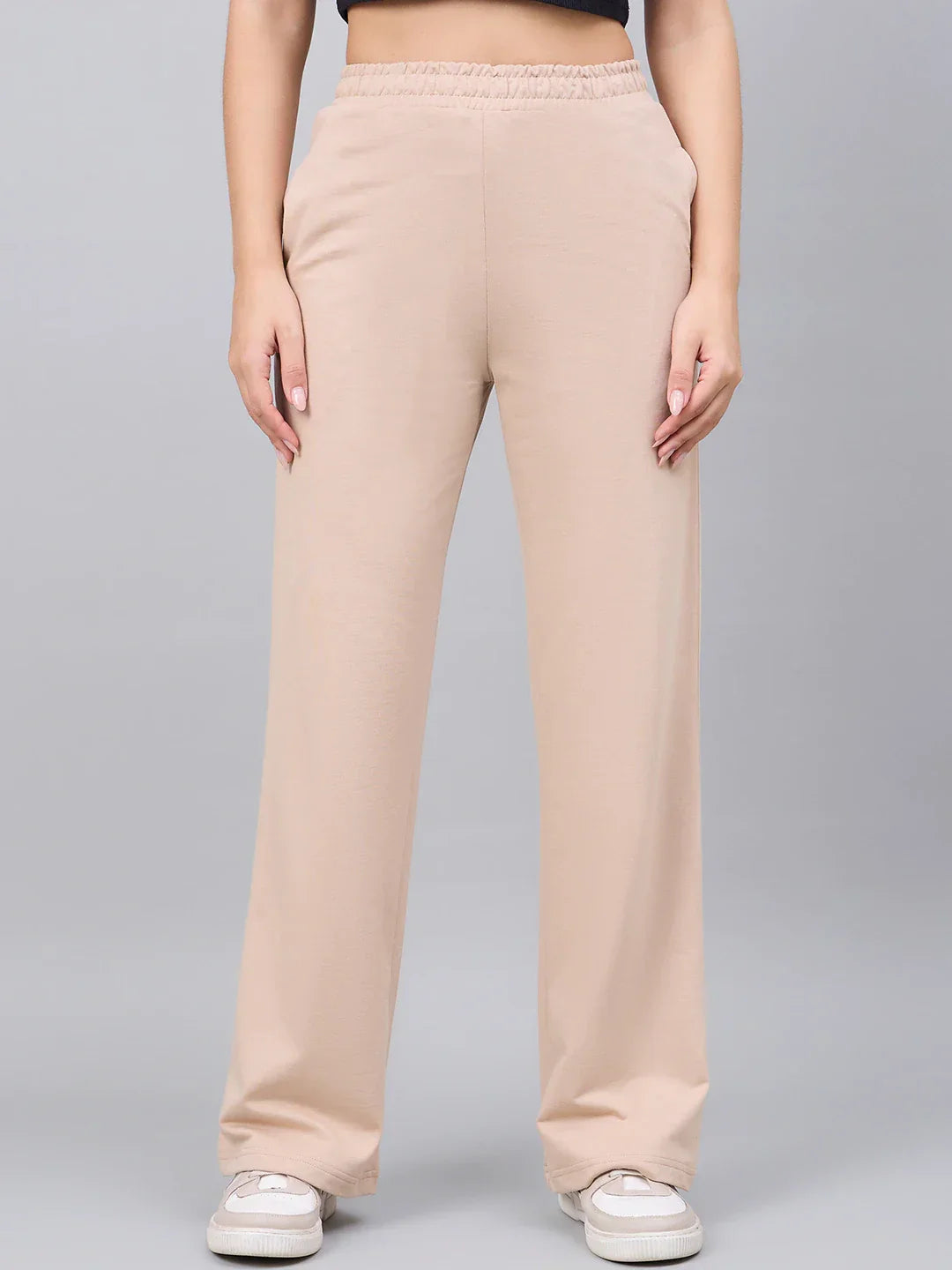 A person wears 98degreenorth Women’s Beige Cotton Stretchable Trackpants, standing against a plain gray background.