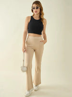 Woman in 98degreenorth beige flared bootcut pants, black crop top, and round purse stands against a plain background.