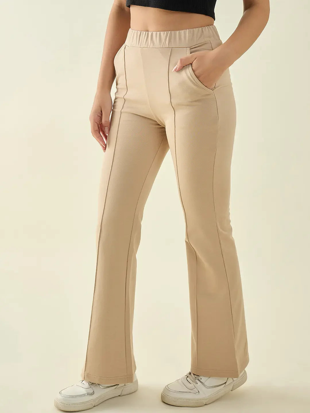 Woman in 98degreenorth Beige Flared Bootcut Cotton Trousers, styled with white sneakers and a black crop top.