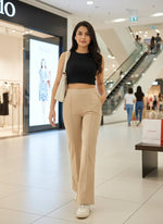 Woman in 98degreenorth beige flared bootcut cotton stretchable trousers walks in a mall holding a white bag.