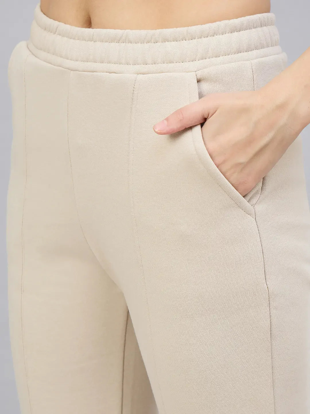 A person wearing 98degreenorth Women’s Beige Flared Bootcut Sweatpants with one hand in the right pocket.