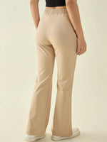 A person in 98degreenorth Women’s Beige Flared Fit Bootcut Cotton Stretchable Trousers stands with their back to the camera.