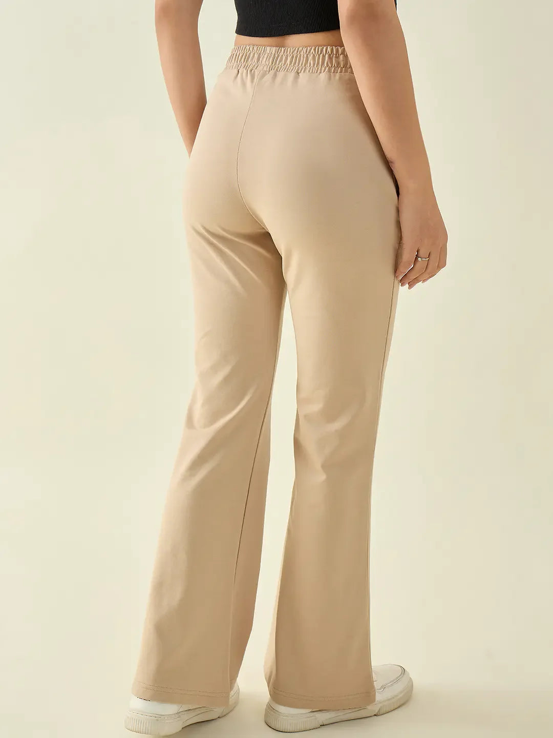 A person in 98degreenorth Women’s Beige Flared Fit Bootcut Cotton Stretchable Trousers stands with their back to the camera.