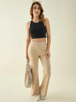 Woman in a black sleeveless crop top, 98degreenorth beige flared bootcut trousers, colorful tote, and white sneakers.