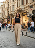 A woman walks down a city street in 98degreenorth Beige Flared Fit Bootcut Trousers and a black crop top.