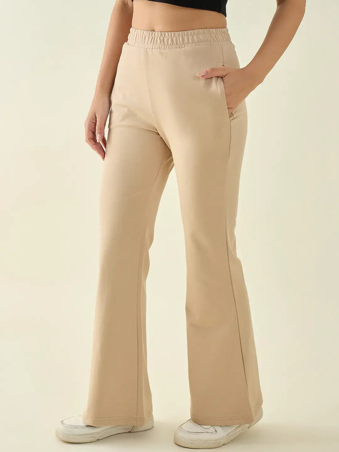 Woman wears 98degreenorth Women’s Beige Flared Fit Bootcut Cotton Stretchable Trousers, white sneakers, black crop top.