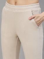 Close-up of a woman wearing 98degreenorth Beige Fleece Flared Lounge Pants with hand in pocket, against gray background.