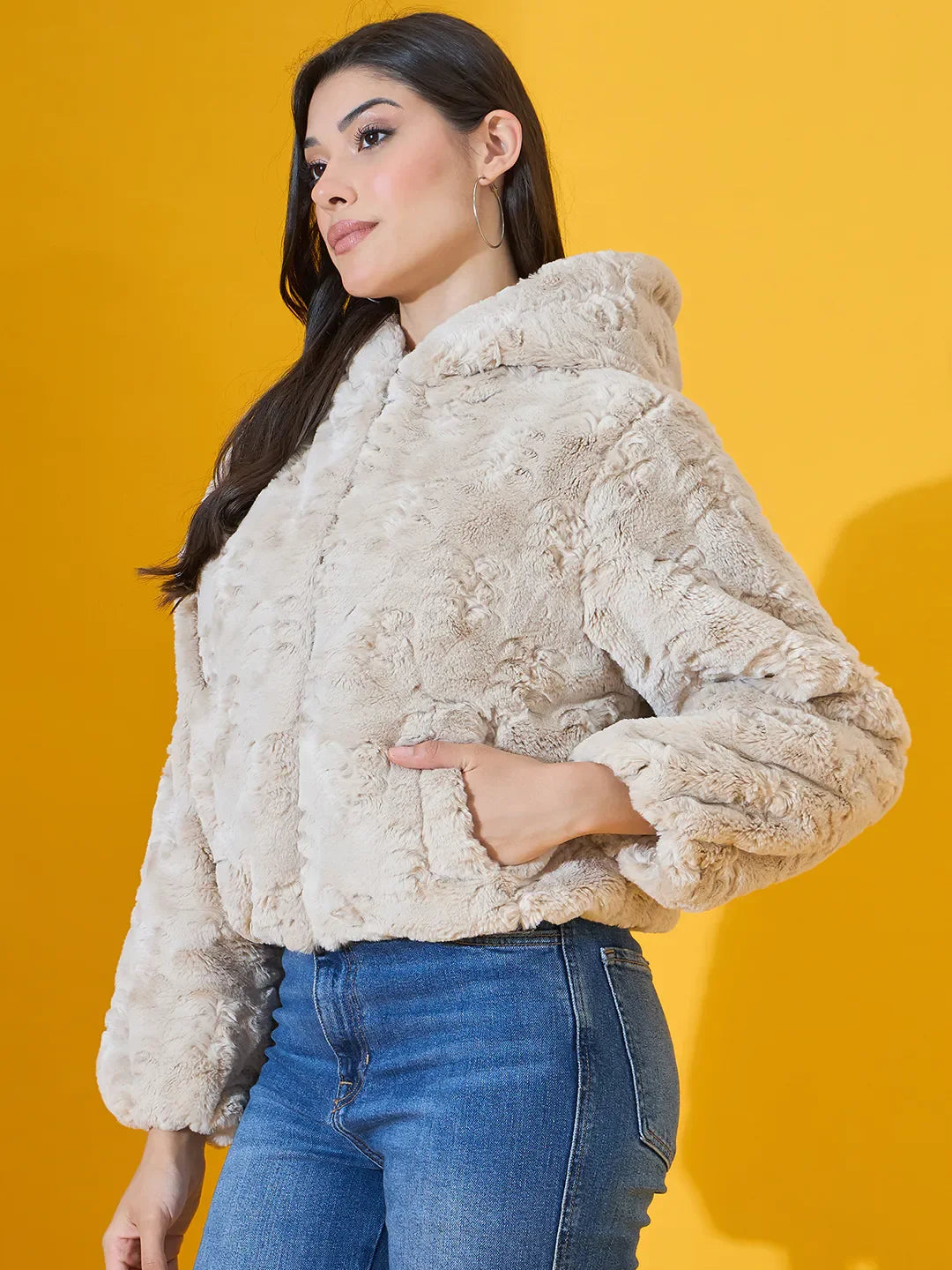 Woman wears 98degreenorth’s Beige Luxe Faux Fur Hooded Jacket, cropped fit, against a solid yellow background.