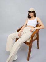Woman in 98degreenorth Beige Multi Bootcut Sweatpants sits relaxed on a wooden chair against a gray background.