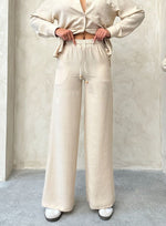 Woman in 98degreenorth Beige Wide Leg Linen Pants with drawstring waist, posing hands on hips against a textured wall.