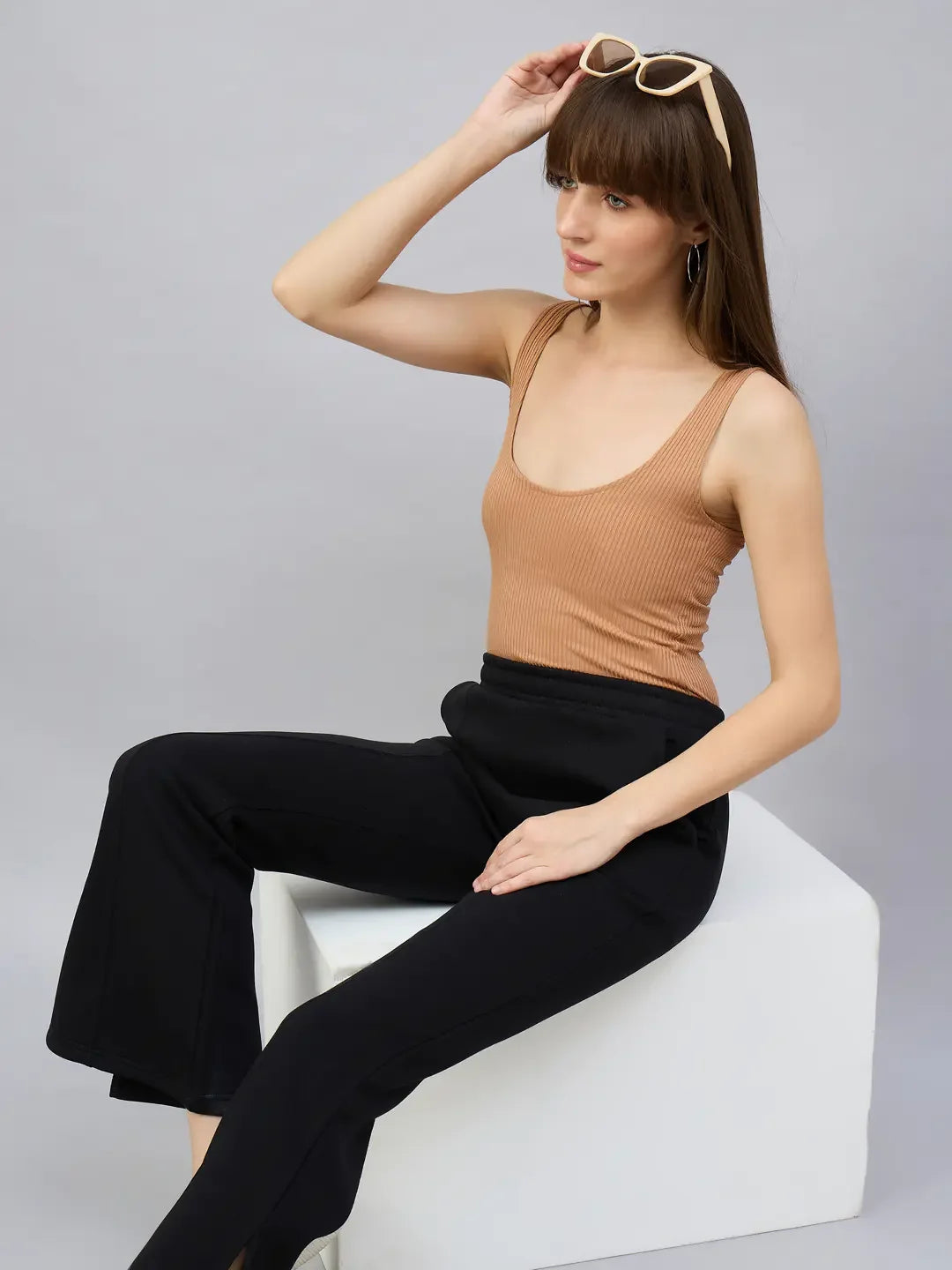 A woman models 98degreenorth Women’s Black Bootcut Sweatpants with Side Slit, sitting on a white block.