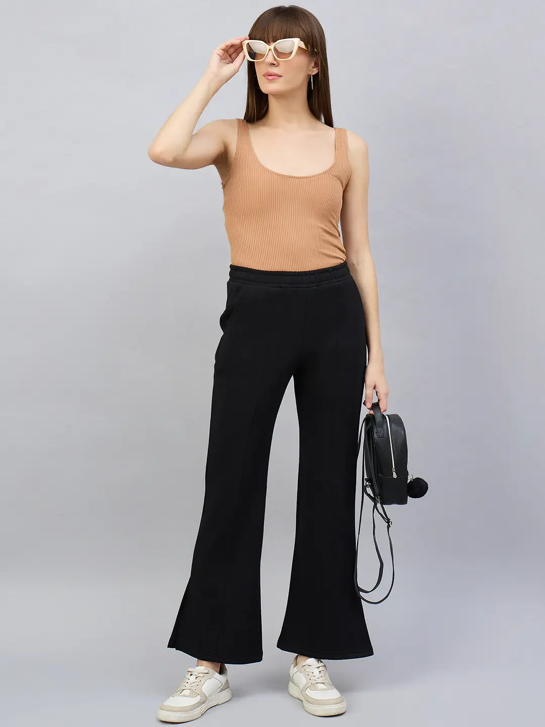 Woman in a tan tank, 98degreenorth black bootcut sweatpants, white sneakers, black bag, and white sunglasses.