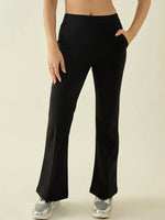 A woman wears 98degreenorth Black Flared Bootcut Cotton Work Pants with silver sneakers, hand in pocket, on plain backdrop.