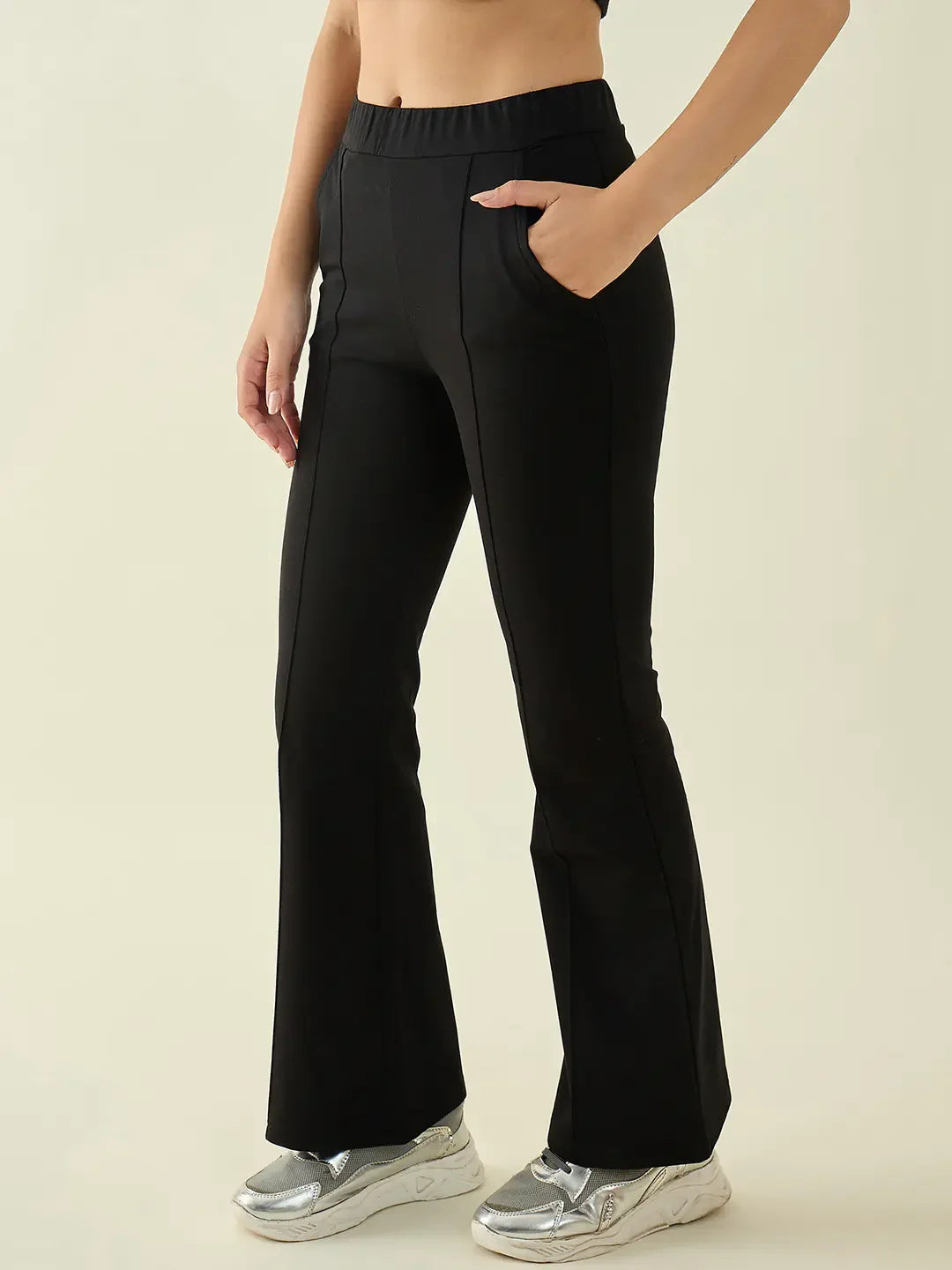Woman wears 98degreenorth Black Flared Bootcut Cotton Stretchable Trousers with silver sneakers, hand in pocket.
