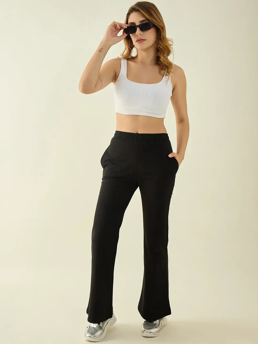 Woman in sunglasses, white crop top, and 98degreenorth black flared fit bootcut trousers stands against a plain background.