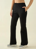 She wears 98degreenorth Women’s Black Flared Fit Bootcut Cotton Trousers with silver sneakers on a neutral background.