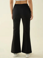 Model in 98degreenorth black flared bootcut trousers and white sneakers, shown from the back against a plain backdrop.