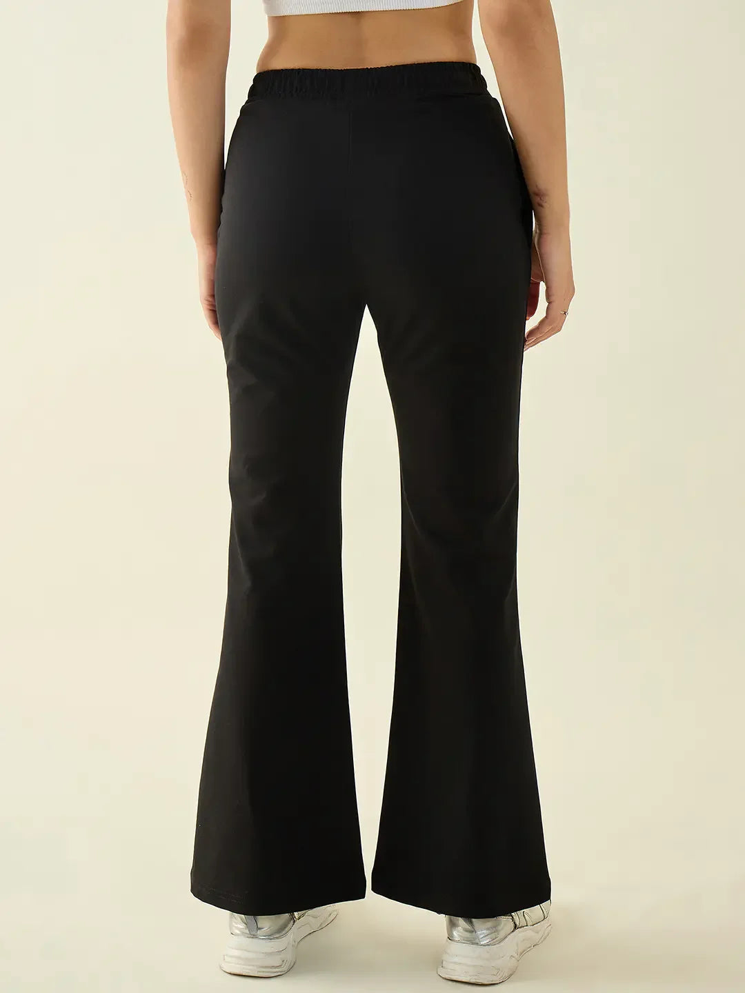 Model in 98degreenorth black flared bootcut trousers and white sneakers, shown from the back against a plain backdrop.