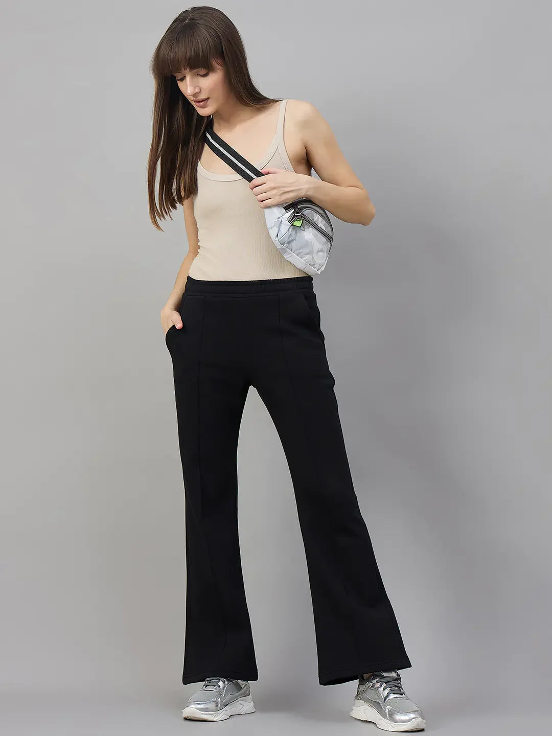 Woman in beige tank, 98degreenorth Women’s Black Fleece Flared Sweatpants, silver sneakers, and crossbody bag.