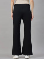 Model wearing 98degreenorth Women’s Black Fleece Flared Sweatpants, shown from the back with white sneakers on gray backdrop.