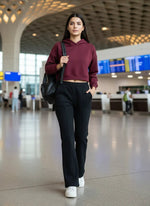 A woman in a maroon hoodie and 98degreenorth Women’s Black Fleece Flared Sweatpants walks through an airport terminal.
