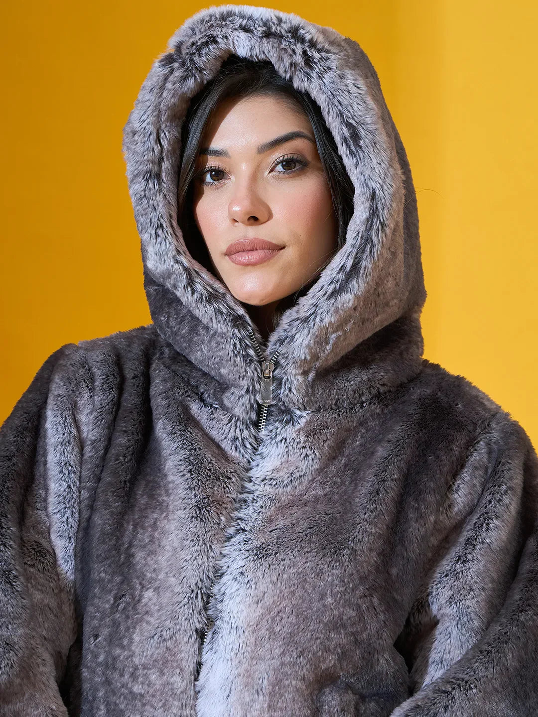 Woman in a 98degreenorth black premium faux fur jacket with hood, standing before a yellow background.