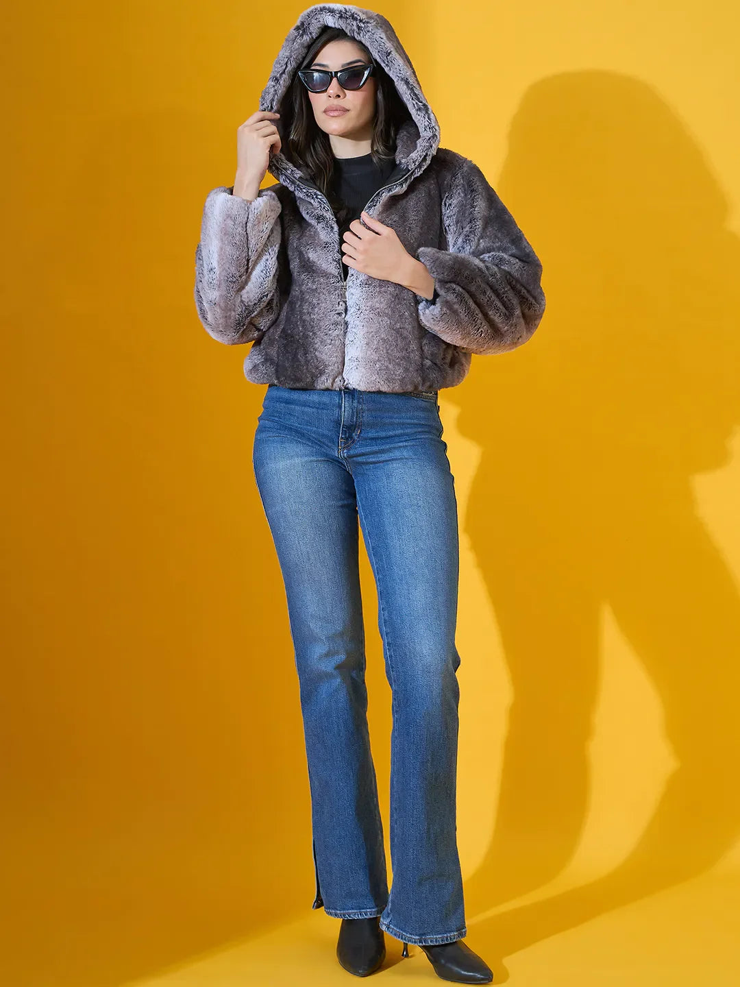 Woman wears 98degreenorth’s Black Premium Faux Fur Jacket with plush hood, posing in sunglasses and blue jeans.