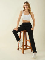 Woman wears 98degreenorth Women’s Black Regular Fit Cotton Stretchable Trousers, seated on a stool against a plain backdrop.