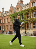 A woman in 98degreenorth Women’s Black Regular Fit Cotton Stretchable Trousers walks on campus with books.