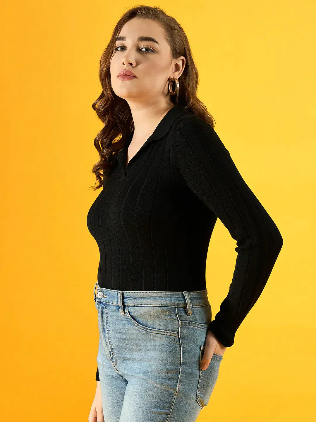 Woman in a 98degreenorth Women’s Black Ribbed Collar Sweater and blue jeans against a vibrant yellow background.