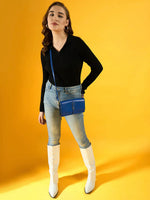 Woman in 98degreenorth Black Ribbed Collar Neck Sweater, blue jeans, white boots & blue purse against yellow background.