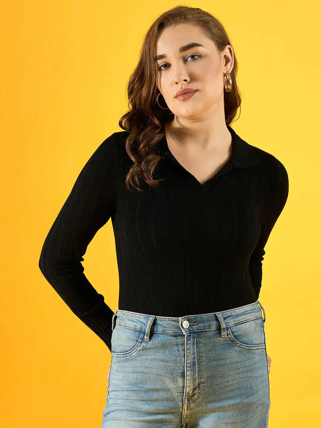 Woman in a 98degreenorth Women’s Black Ribbed Collar Neck Sweater, slim fit, with blue jeans against yellow background.