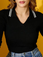 Woman in a 98degreenorth black ribbed collared knit sweater, wearing blue jeans, stands against a yellow background.