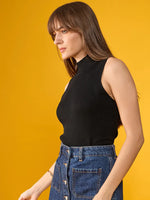 Woman in a 98degreenorth black ribbed high neck sleeveless knit top and denim skirt stands against a yellow background.