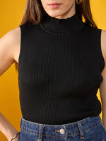 Woman wears 98degreenorth’s black ribbed high neck sleeveless slim fit knit top with blue jeans, against a yellow background.