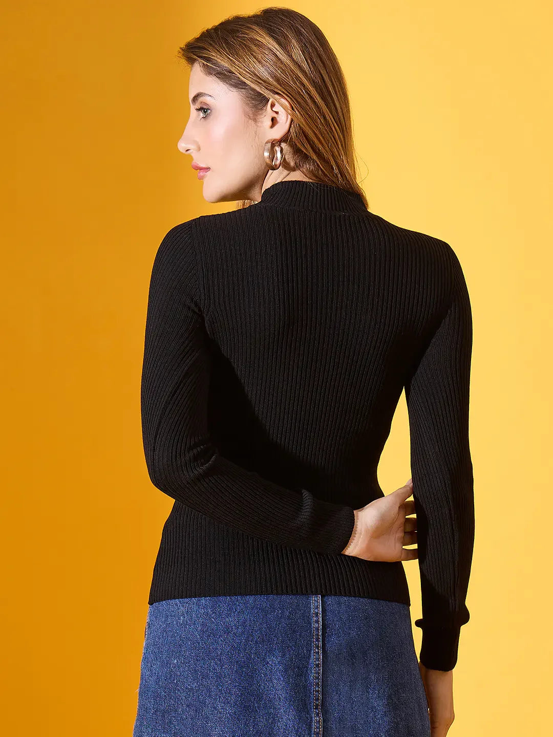 Woman wears 98degreenorth black ribbed high-neck slim fit sweater, facing away against a yellow background.